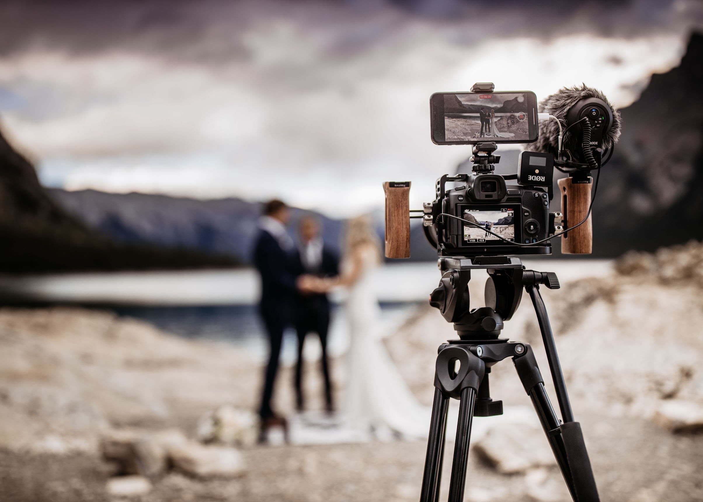 A phone on a camera rig live streaming a couple's elopement ceremony by a mountain lake