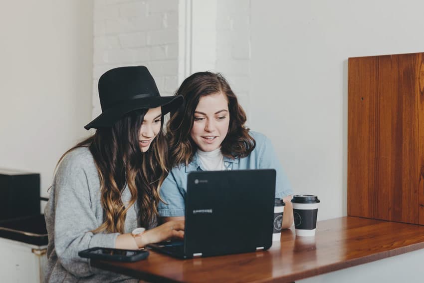 Two friends watching a live stream together on a laptop at a café table