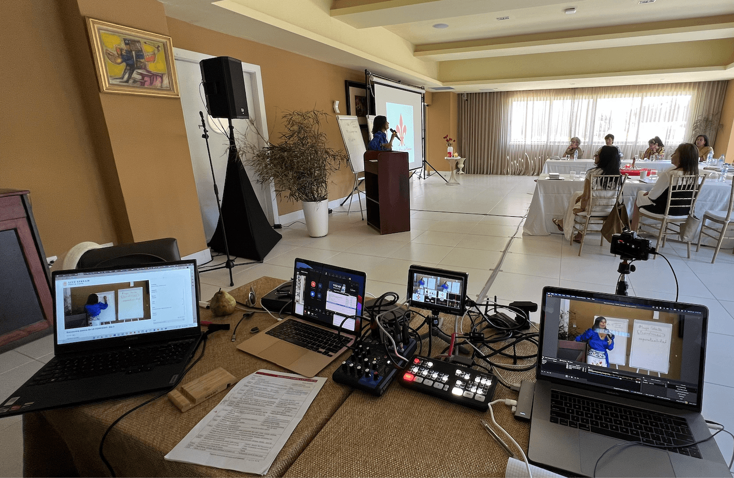 A streaming company's production table at a workshop: laptops, a video switcher, an audio mixer and a camera on a tripod facing the speaker