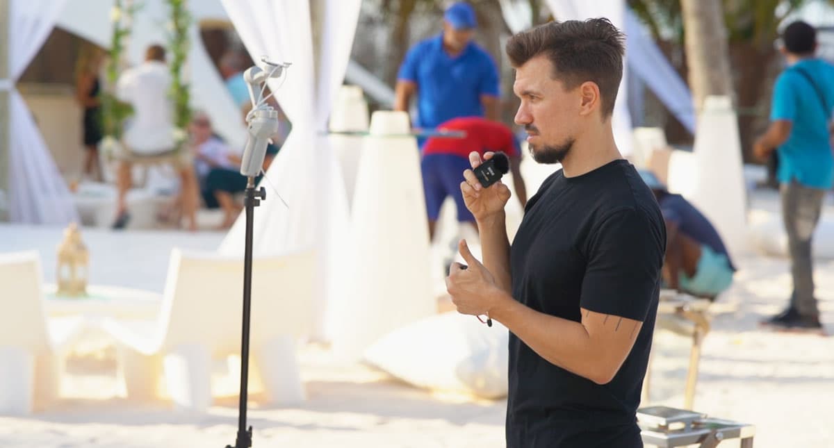 A man testing a wireless microphone next to a phone on a stand before a beach wedding